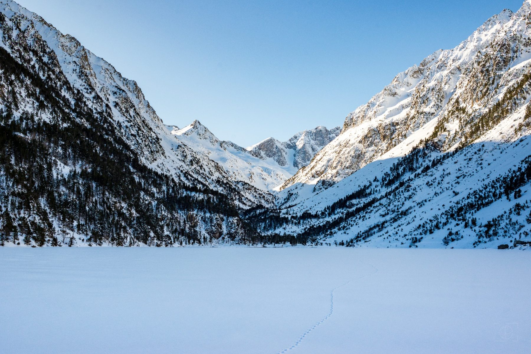 Lac de Gaube d'Hiver — collection Paysages — Une empreinte solitaire trace son chemin sur l'immensité blanche d'un lac gelé, niché au cœur d'un écrin de montagnes enneigées baignées de silence. — tirage d'art photographique en édition limitée par Sébastien Pontico
